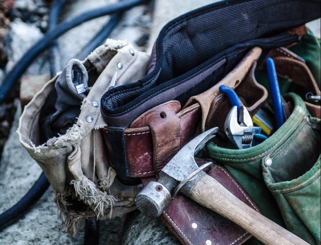 An image of a tool belt with a hammer, wrench, gloves, and other tools. What to include on my tool belt. Toolbox Essentials.
